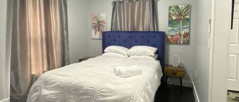 A bedroom with a bed, curtains, a nightstand, and wall art.