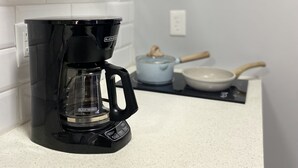 A kitchen with a coffee maker, a pot on the stove, and a plant on a shelf.
