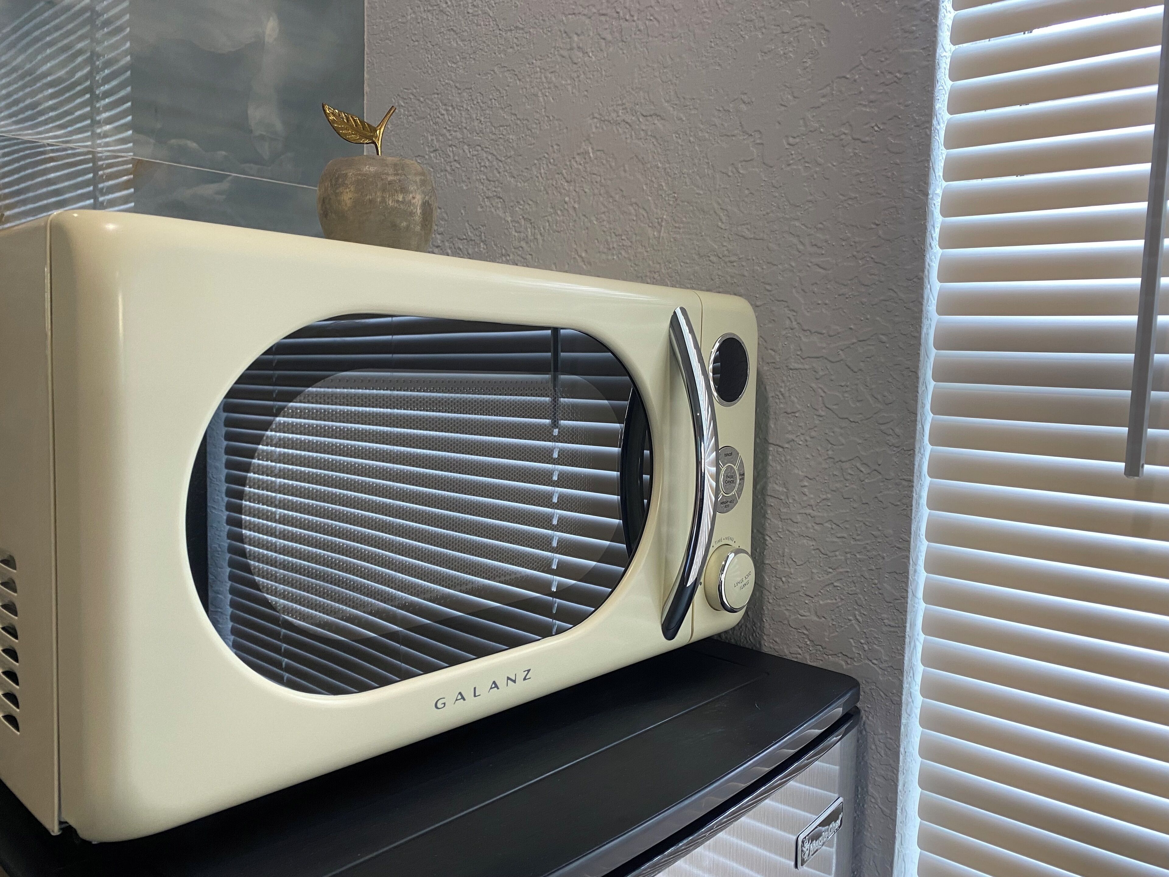 Une radio Galanz vintage, posée sur une étagère noire, devant un mur à la texture particulière.