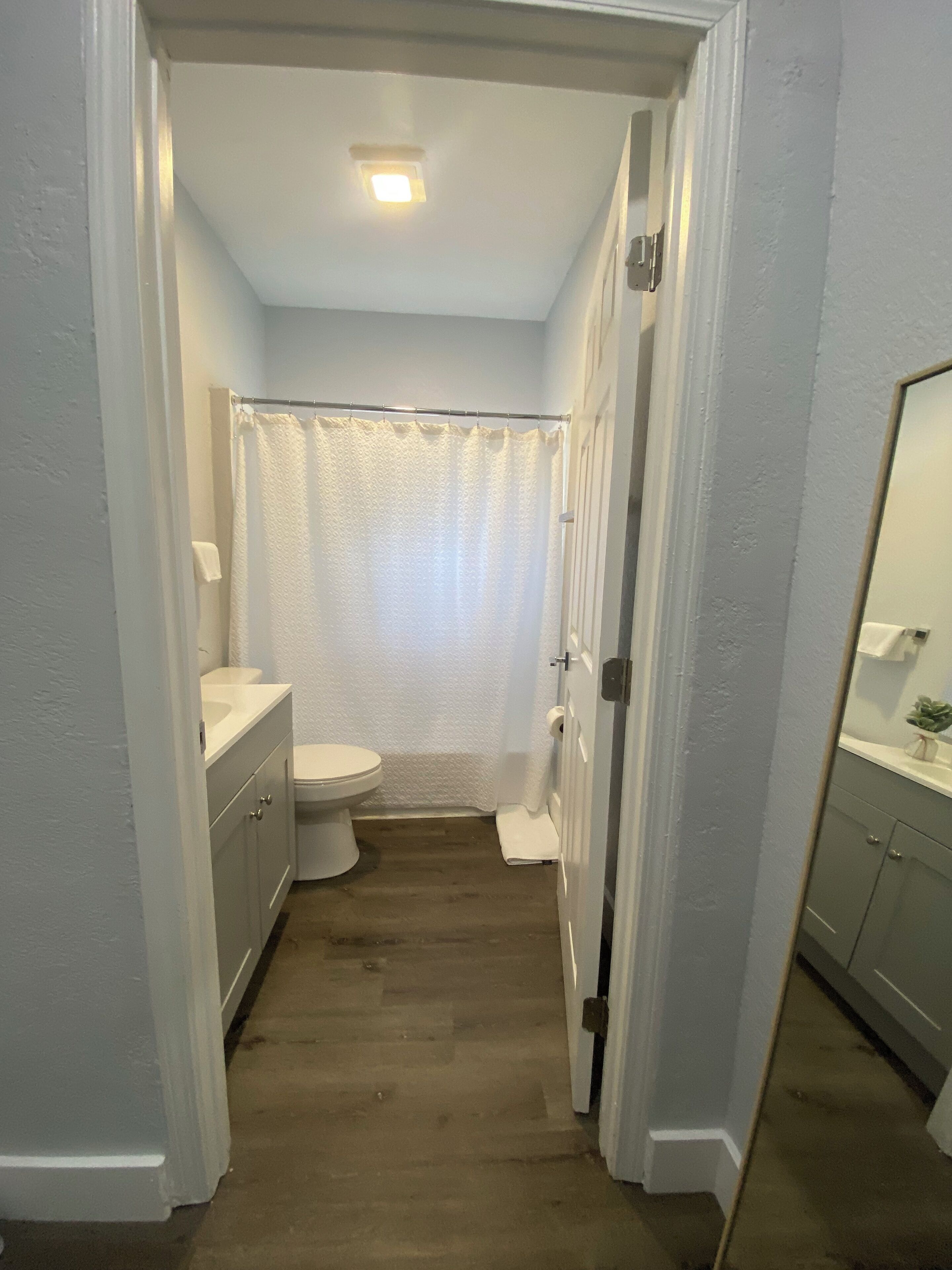 A narrow hallway leading to a bathroom with a toilet, a sink, and a shower curtain.