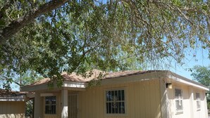 A small, single-story building with a sloped roof, a porch with a railing, and a window with decorative bars. - Texas themed cabin with a Shared fishing pier Not waterfront (Rio Hondo)