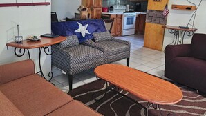 A living room with a sofa, a coffee table, and a TV. There is a kitchen in the background with wooden cabinets and a stove. - Texas themed cabin with a Shared fishing pier Not waterfront (Rio Hondo)