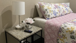A neatly arranged bedroom with a bed, a bedside table with a lamp, a remote control, and a vase with flowers. - The Cherry Blossom (Sanford)