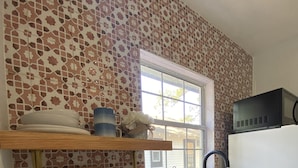 A kitchen with a patterned backsplash, a window, a microwave, and a sink. - The Cherry Blossom (Sanford)