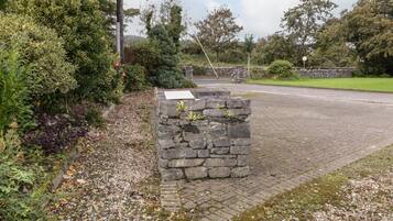 A stone wall with a plaque, surrounded by greenery and a paved path.