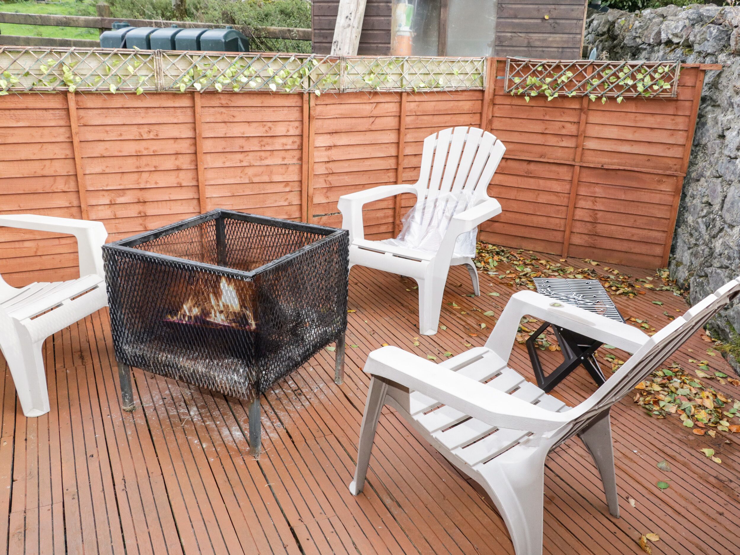 Un patio con un brasero de metal, sillas de plástico blanco y una terraza de madera.