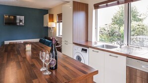 Une cuisine moderne avec un îlot central en bois, un lave-linge et une grande fenêtre donnant sur un paysage verdoyant.