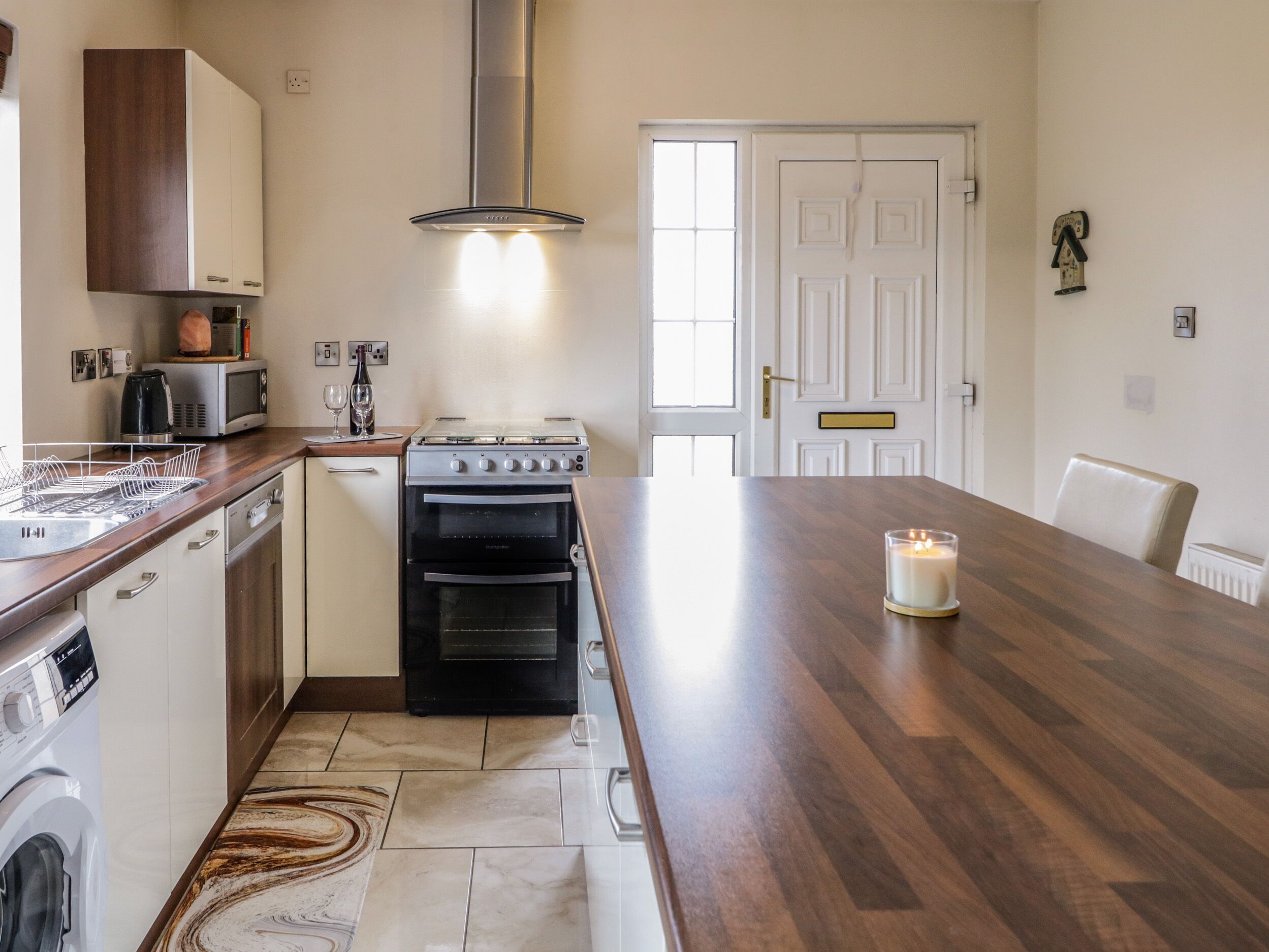 A kitchen with a stove, oven, microwave, and dishwasher. There is a wooden countertop, a rug, and a candle on the table.