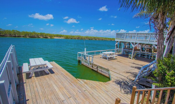 A wooden dock extending into a calm body of water, with a covered seating area and a small building with a balcony. - EMMA’S COTTAGE; WATERFRONT FISHING PIER (Rio Hondo)