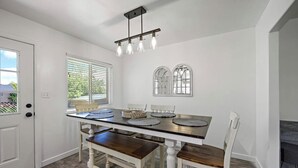A dining area with a white table, four chairs, a chandelier, and a window with blinds. - Home in Kanab with Game Room. Sleeps 10, Pets OK! (Kanab)