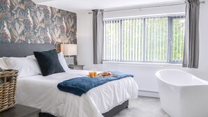 A modern hotel room with a large bed, a bathtub, and a window with blinds. - 4 bedroom accommodation in Bridlington (Bridlington)