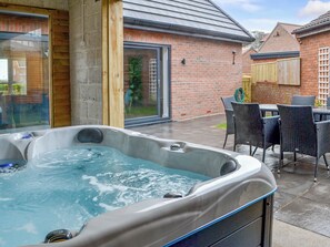 A hot tub in a covered outdoor area with a brick wall and a glass door.