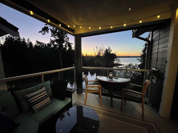 A balcony with a view of the water, a table, chairs, and a sofa.