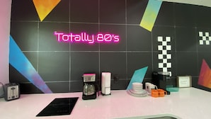 Una cucina con un neon che riporta la scritta “Totally 80's”, una macchina del caffè, un bollitore, un tostapane e un forno a microonde sul bancone.