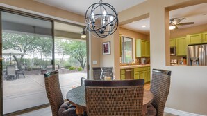 A dining area with wicker chairs and a round table, a kitchen with green cabinets, and a view of the outdoors. - Snowbirds Welcome! Anthem Gem w/ Fairway Views (Anthem)