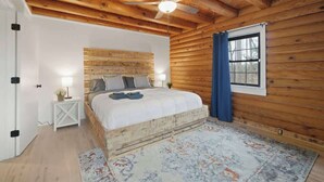 Een slaapkamer met een houten hoofdeinde, een bed met kussens, een nachtkastje met een lamp, een raam met gordijnen en een plafondventilator.