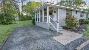 A single-story house with a porch, a front yard with a gravel driveway, and a small garden area. - Abbott Park 5 minutes to South End- 2 BR (Charlotte)