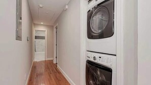A laundry room with stacked washers and dryers, a wooden floor, and a white door at the end of the hallway. - Abbott Park 5 minutes to South End- 2 BR (Charlotte)