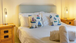 A neatly made bed with white linens, two bedside tables with lamps, and decorative pillows with sailboat designs. - Longbeach meets all your needs for a coastal family retreat. (Beadnell)