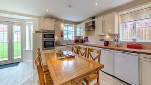 A modern kitchen with a dining area, featuring stainless steel appliances, wooden furniture, and a view of the backyard. - Longbeach meets all your needs for a coastal family retreat. (Beadnell)