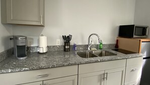 Eine Küche mit Granitabdeckung, Spüle aus Edelstahl und weißen Schränken. Auf der Arbeitsplatte befinden sich eine Kaffeemaschine, ein Papierhandtuchhalter und eine Mikrowelle.