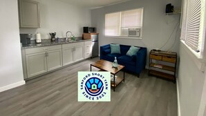 Ein kompakter Wohnbereich mit Küchenzeile, einem blauen Sofa, einem Couchtisch und einem kleinen Holztisch.