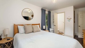 A bedroom with a bed, bedside table, lamp, and a round mirror on the wall. - Comfy cozy laid back cottage (Charlotte)
