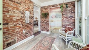 A room with a brick wall, a white wicker chair, a hanging plant, and a large window. - Comfy cozy laid back cottage (Charlotte)