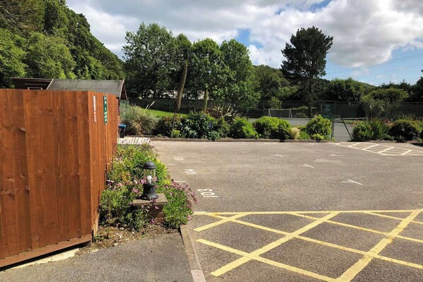 A parking lot with yellow crosshatched markings, surrounded by greenery and a wooden fence.