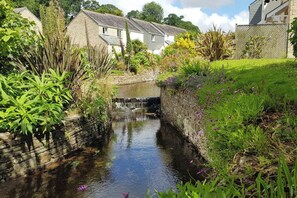 A narrow water channel with a small waterfall, surrounded by stone walls and lush greenery.