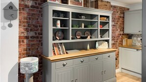 Una cocina con un mueble gris, encimera de madera y pared de ladrillo.