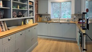Una cocina con armarios grises, encimera de madera y ventana con persianas decorativas.