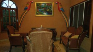 Quarto com uma mesa de jantar de madeira, duas poltronas e um sofá. Há duas decorações de papagaios coloridos na parede.