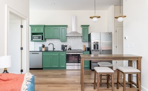 A modern kitchen with green cabinets, stainless steel appliances, and a wooden dining table with four chairs. - Luxurious Nulu Stay - Ideal for Big Groups (Louisville)