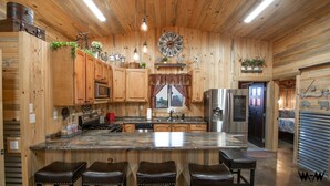 L’intérieur d’un chalet en bois comprend une cuisine, des tabourets de bar, une horloge et une pancarte de bienvenue.