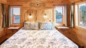 Une chambre à coucher dans une cabane en bois, avec un lit, deux fenêtres et un médaillon décoratif au plafond.