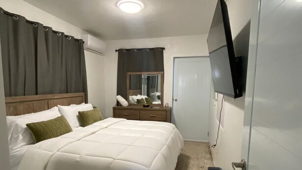 A bedroom with a bed, bedside table, mirror, TV, and a door. - Juana Diaz Spacious Cozy Home Mango trees and avocado. (San Juan)