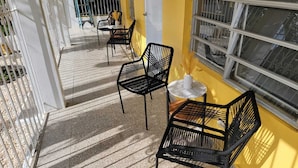 A sunlit outdoor seating area with metal chairs and a small table, surrounded by a white fence and a yellow wall. - Juana Diaz Spacious Cozy Home Mango trees and avocado. (San Juan)