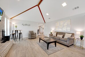 A spacious living room with a high ceiling, a fireplace, a sofa, a coffee table, and a TV.