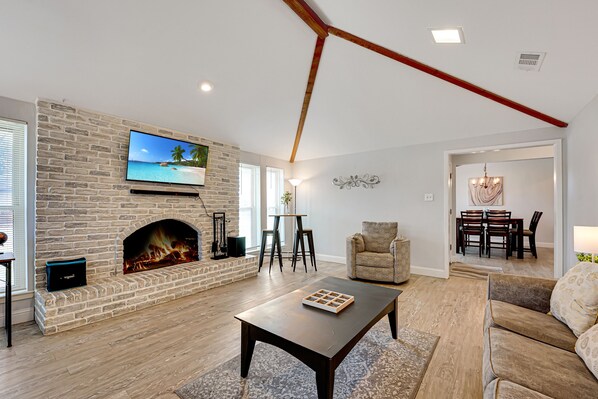 A living room with a stone fireplace, a flat-screen TV, a wooden coffee table, and a sofa.