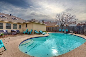 A backyard with a swimming pool, blue lounge chairs, and a wooden fence.