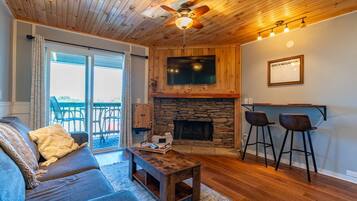 A cozy living room with a stone fireplace, a ceiling fan, and a bar area with stools.
