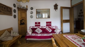 Una sala de estar acogedora con un sofá de madera, un mueble de madera, un espejo y una mesa de comedor con un mantel individual rojo.