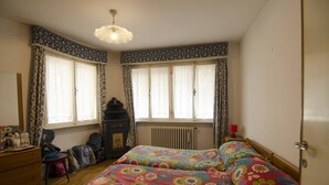 Un dormitorio con un aparador de madera, dos camas con ropa de cama floral, un radiador y una ventana con cortinas estampadas.