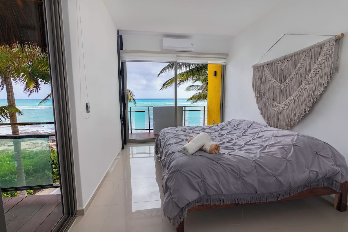 Ein Schlafzimmer mit einem Bett, einer Wanddekoration aus Makramee und Blick auf den Ozean.