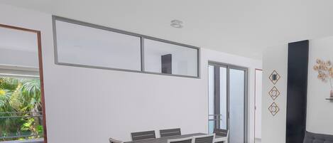 Una sala de estar moderna con comedor, ventanas amplias y vistas a zonas verdes.
