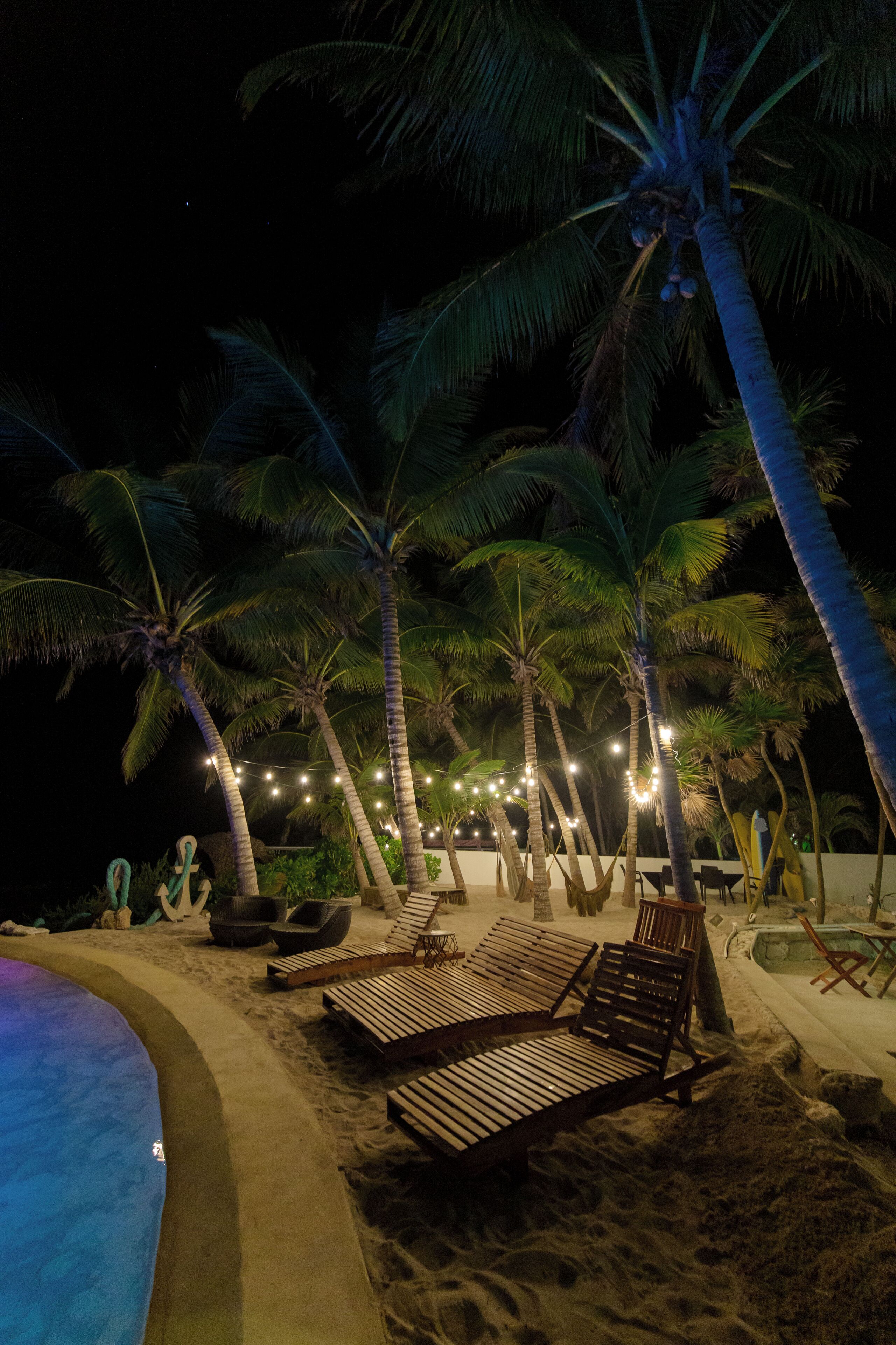 A beach with palm trees, a pool, and lounge chairs.