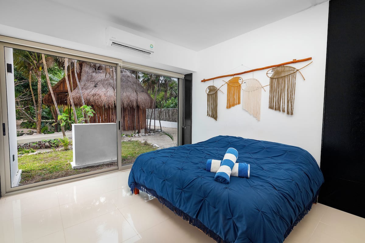 Ein Schlafzimmer mit einem großen Bett, einer Schiebetür zu einem Garten und einer Wanddekoration aus Makramee.