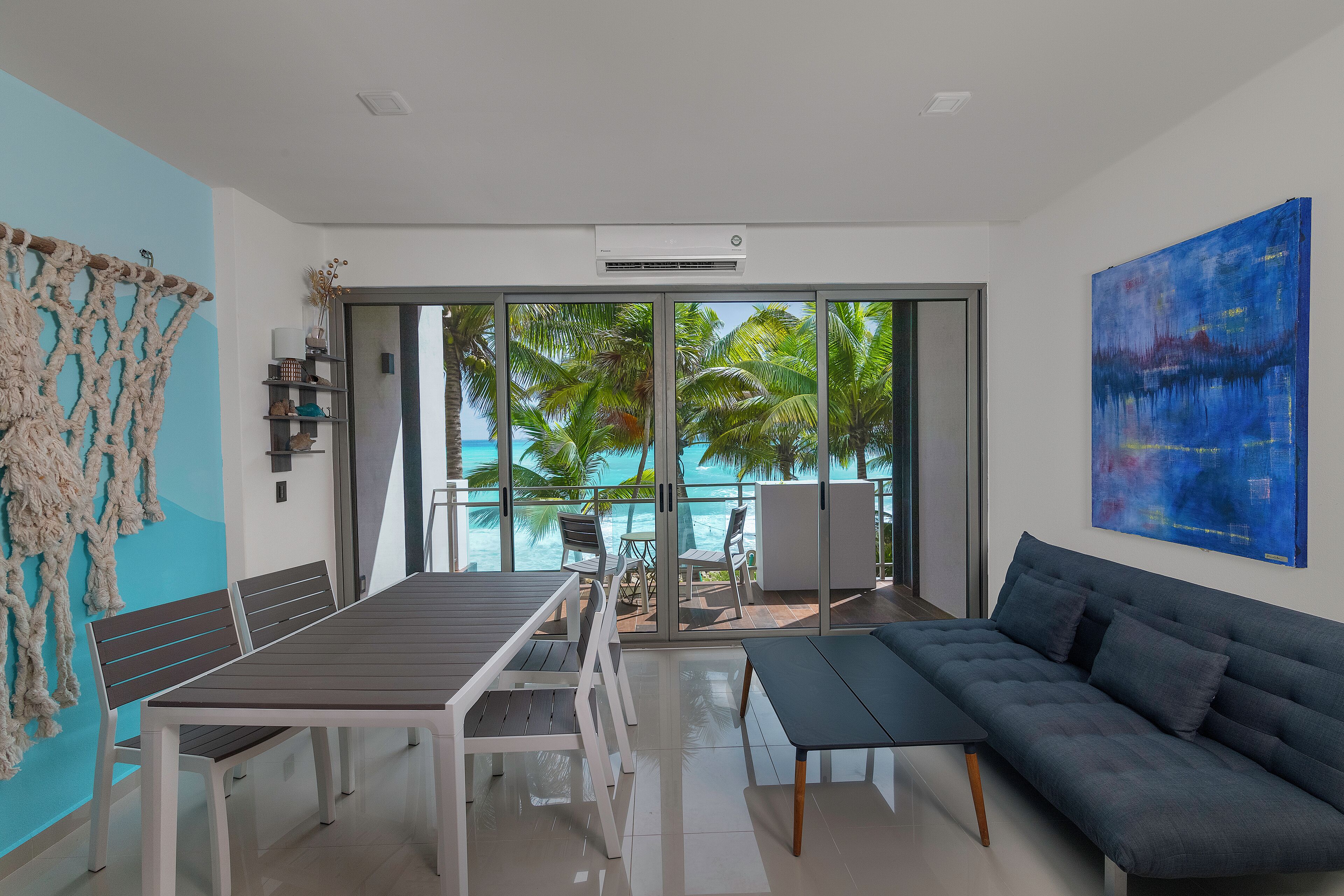 A modern living room with a dining area, a sofa, and a view of a pool and palm trees.