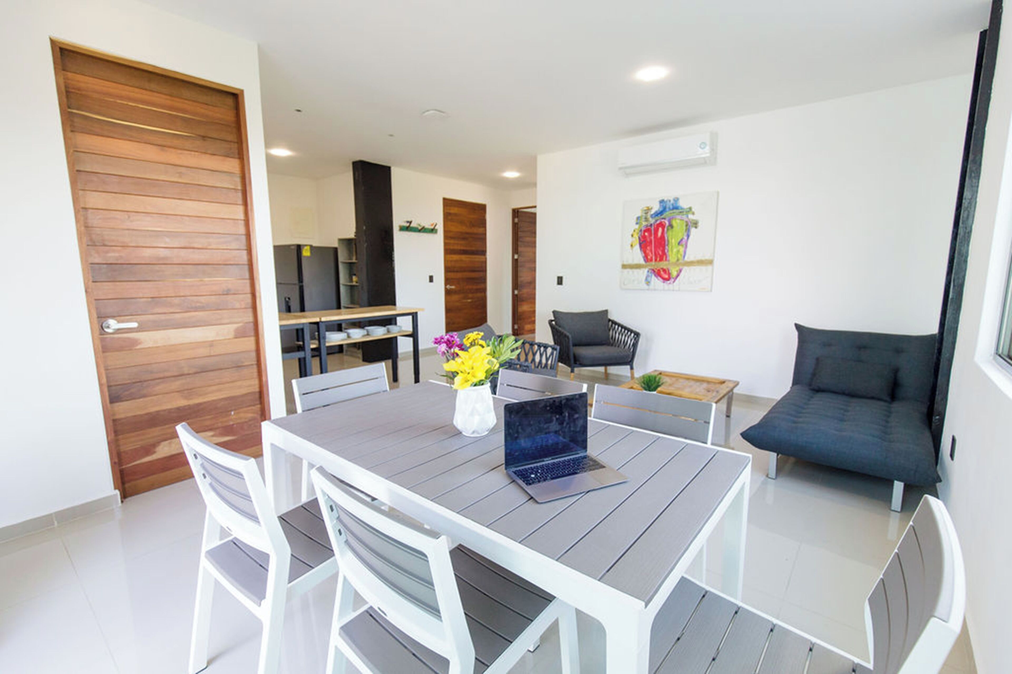 A modern living room with a dining table, chairs, a sofa, and a laptop.